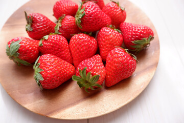 Fresh strawberries on wooden plate. ripe red strawberries on white wooden background. Fresh seasonal fruits. 