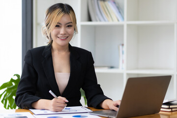 Portrait of attractive young business woman working with laptop and documents on office desk.