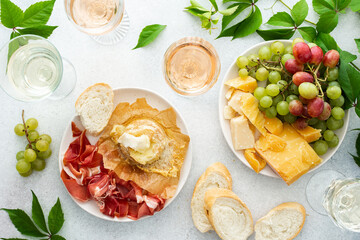 Top view of table with rose and white wine in glasses, plates with grapes, cheese and jamon, baked camembert cheese and baguette, tasting party or cozy dinner with wine