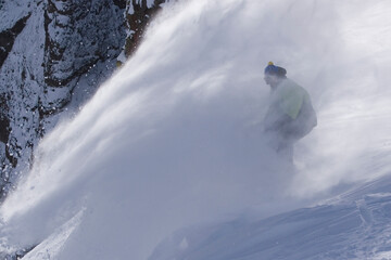 A man snowboarding powder snow on a windy day at Kirkwood ski resort in California