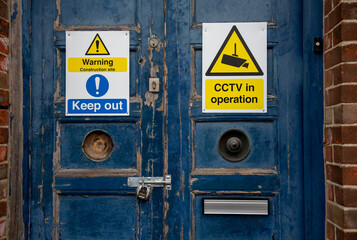 Old large blue wooden door with yellow security and warning signs and old rusty locks 