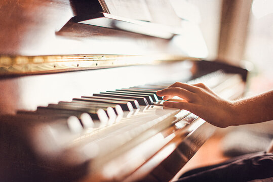 Cropped image of child's hand playing piano in a sunny room.