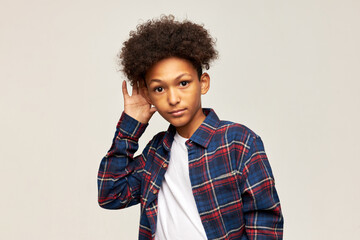 Studio image of astonished boy kid in flannel shirt and with afro haircut eavesdropping with...