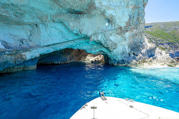 Tourists on an excursion boat explore the inside of a sea grotto flooded with sunlight, surrounded...