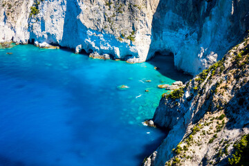 Fototapeta premium Beautiful crystal clear blue and turquoise waters next to a rugged, overgrown coastline that makes a wonderful play of colors, Keri, Zakynthos, Greece
