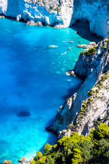Fototapeta premium Beautiful crystal clear blue and turquoise waters next to a rugged, overgrown coastline that makes a wonderful play of colors, Keri, Zakynthos, Greece