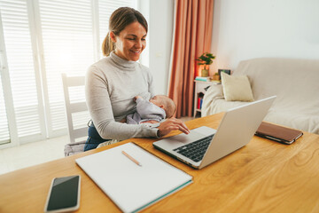 Young mother working at home while feeding her infant son - Smart working and family concept - Focus on mom face - obrazy, fototapety, plakaty