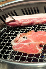 Grilling pork belly meat on a round BBQ net in restaurant for eating.