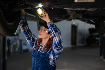 A female mechanic inspects a lifted car. A girl at a man's work.