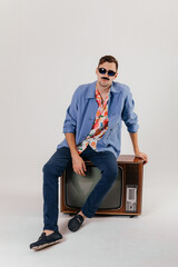 Back in time 90s 80s lifestyle concept. Studio footage of stylish cheerful young man in vintage retro jacket with antique old tv, candy-colored fashions, creativity, emotions, facial expression