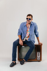 Back in time 90s 80s lifestyle concept. Studio footage of stylish cheerful young man in vintage retro jacket with antique old tv, candy-colored fashions, creativity, emotions, facial expression