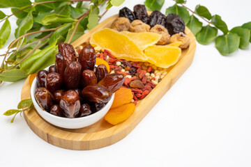 Wooden dish with dates, dried apricots, nuts, mangoes, figs and prunes on a background of green leaves