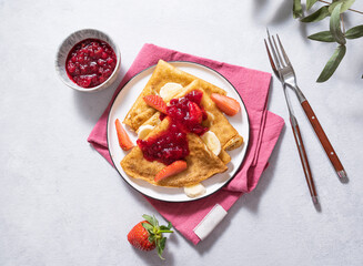 Sweet pancakes with berry jam, strawberries and banana on a light background. The concept of homemade healthy food.