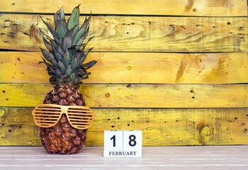 Creative planner calendar February with number  18. Pineapple character on bright yellow summer wooden background with calendar cubes.