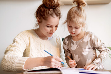 Cute girl spends time at home with her mother  drawing in a sketchbook