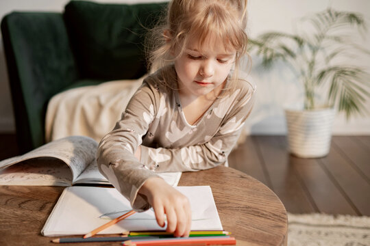 Cute little girl drawing with pencils sitting at the children's table in a bright room