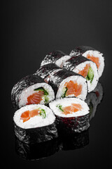 futomaki sushi roll with cucumber salmon cream cheese on a black mirror background © Narsil