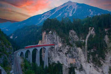 Photo sur Plexiglas Viaduc de Landwasser A local train of Rhaetian Railway coming out of the tunnel in a cliff crossing famous Landwasser Viaduct over a deep gorge with fall colors on the rocky mountainside in Filisur, Grisons, Switzerland