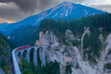 Photo sur Plexiglas Viaduc de Landwasser A local train of Rhaetian Railway coming out of the tunnel in a cliff crossing famous Landwasser Viaduct over a deep gorge with fall colors on the rocky mountainside in Filisur, Grisons, Switzerland