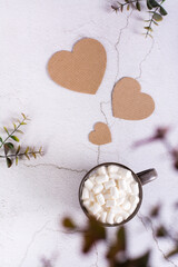 Latte with marshmallows in a cup and a cardboard hearts on a gray table. Top and vertical view