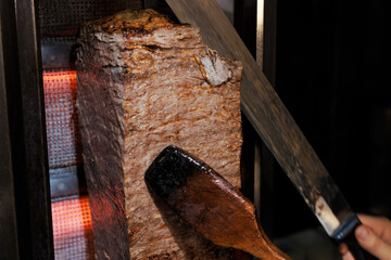 Fototapeta premium Traditional Turkish doner kebab I gyro grilled in gas fired oven. Famous doner kebab from Turkish cuisine in restaurant. Man slicing doner kebab to serve.