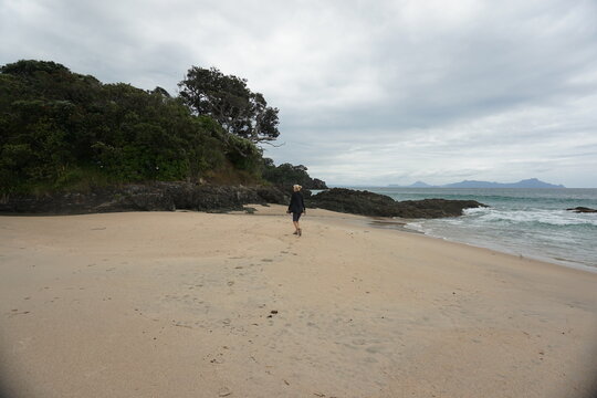 A blonde woman walking and taking pictures around Langs beach in New Zealand.