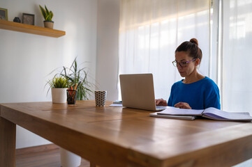 Side view of caucasian brunette woman working at home on her laptop.