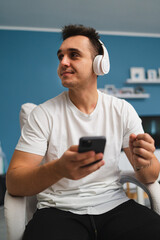 A young guy is using his phone and drinking coffee from his working chair in his house during the day