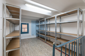 Spacious room with good lighting on ceiling and laminate flooring. Along walls are metal shelving with wooden shelves for storage. Solution for freeing up space, storing property at home.