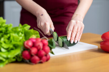 Close-up photo of slicing cucumber by woman in red apron preparing food