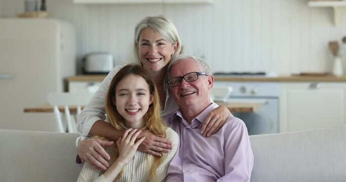 Portrait of multi generational family, old man, grown up daughter, pretty teenager granddaughter sit on sofa smile look at camera. Adolescent girl and mother visit their mature relative. Family ties