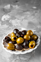 Delicious black and green olives in plate on gray background