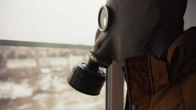 waiting for a nuclear catastrophe. a man in a gas mask looks out the window