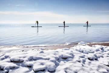 Man is paddling on sup board in the winter ice lake