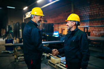 Mechanical engineers shaking hands in factory.