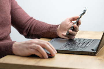 Close up of a man working on laptop and using smartphone. Businessman using smartphone while working on laptop in the office on a desk