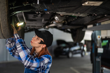 A female mechanic inspects a lifted car. A girl at a man's work.