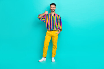 Full size photo of optimistic guy brunet haircut wear colorful shirt showing thumb up hand in pocket isolated on teal color background