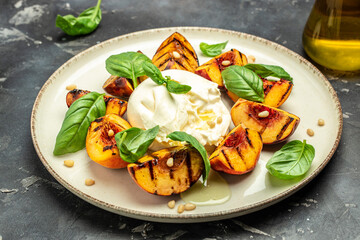 Burrata soft cheese and grilled peaches with basil and pine nuts, drizzled honey, Food recipe background. Close up