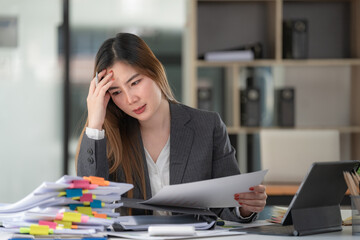 Sad Asian woman looking annoyed and stressed, sitting at the desk, using a laptop, thinking, feeling tired and bored with depression problems.