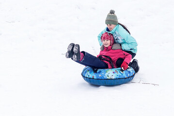 Fototapeta na wymiar Two happy girls-sisters ride down a winter slide on a children's tubing 