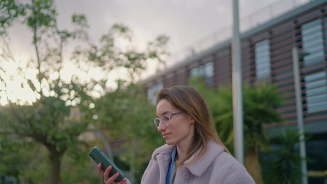 young hipster woman walking around an urban park with her bicycle and checking her social networks on a smartphone. Female wearing glasses reading messages on her smartphone