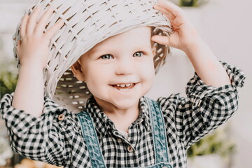 Little girl 1 years old with a basket on her head. Funny child plays puts a basket on her head like a hat and laughs, she is dressed in a plaid shirt and denim overalls. Funny moments with kids.