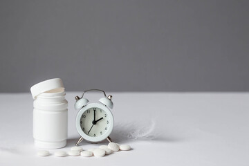 A tube of pills and an alarm clock. The time on the clock is 2 am. Insomnia and recovery of sleep...