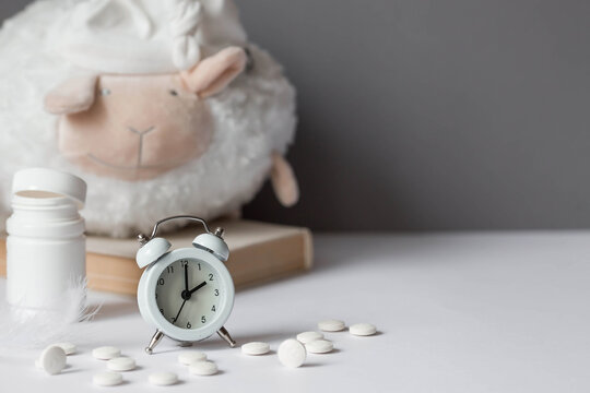 A tube of pills, a sheep in a sleep cap and an alarm clock. The time on the clock is 2 am. Insomnia and recovery of sleep mode. Count sheep to fall asleep.