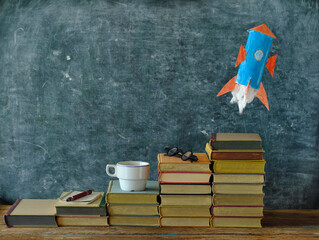 Stack of hardback books with rocketship launching on blackboard...