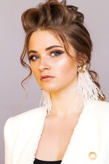 Long white ostrich feather earrings on a brunette girl in a white jacket. Girl posing on a gray background