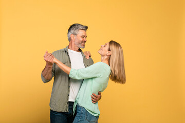 Loving middle aged spouses dancing and having fun over yellow studio background, free space