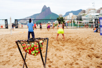 tennis balls in a basket on the beach with people playing beach tennis in the background in Ipanema