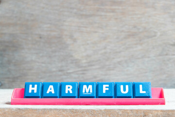 Tile alphabet letter with word harmful in red color rack on wood background